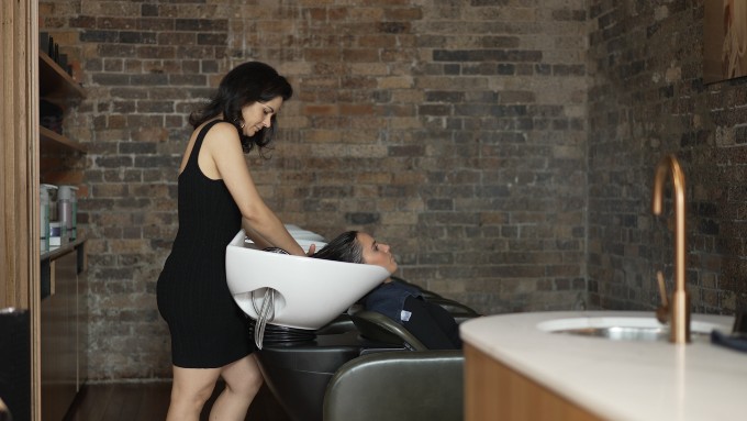 A stylist washing client's hair at the basin.