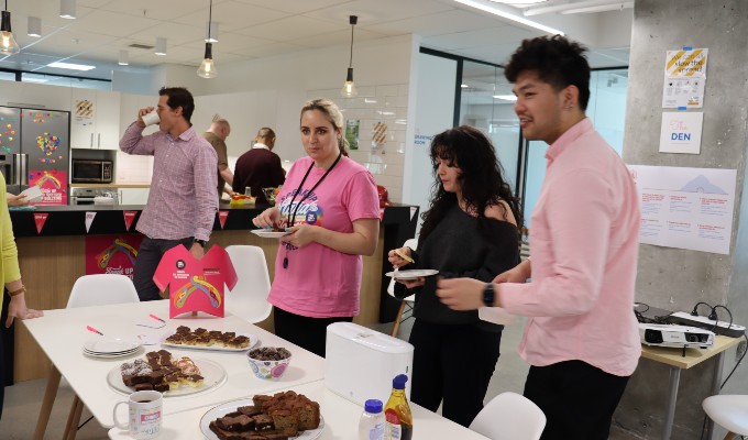 A group of people wearing pink shirts and t-shirts and eating cakes