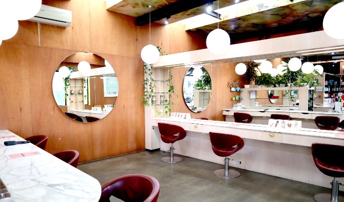 Hair stylist seating in a well-lit space with a round mirror on a wall