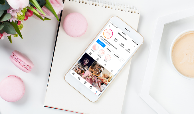 Instagram opened on a smartphone lying on top of a notepad next to a pink macaroon and pink tulips