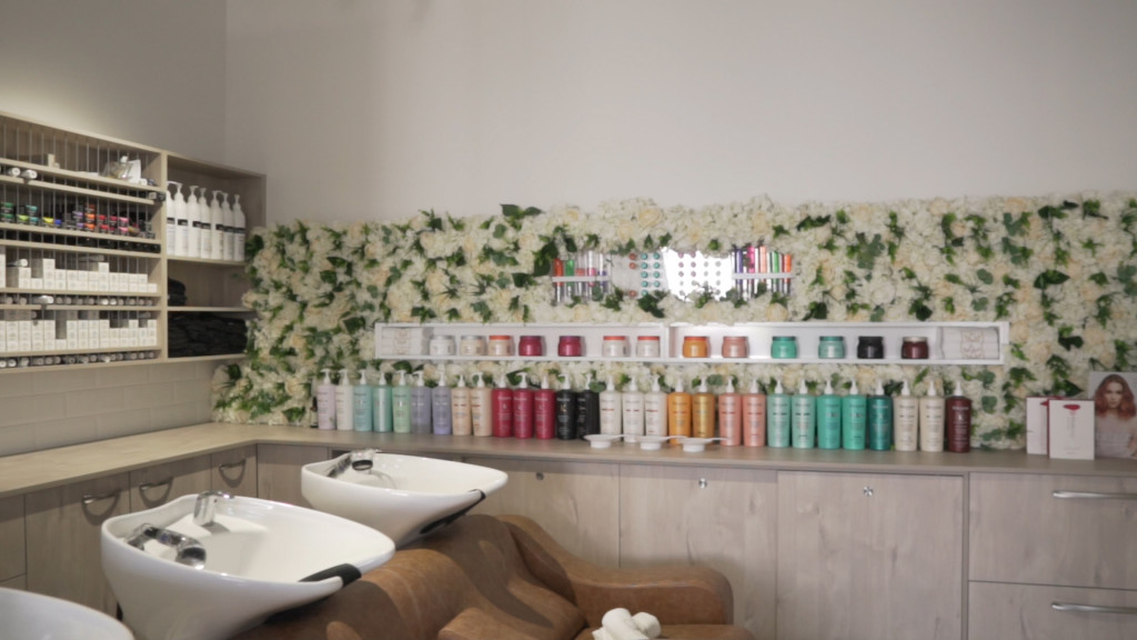 beauty products lined up on shelf wall by hair washing station in salon